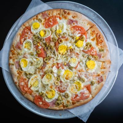 Portuguese pizza topped with mozzarella, ham, tomatoes, green olives, and egg.