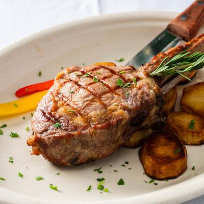 Grilled veil chop with rosemary on a plate with roasted potatoes.