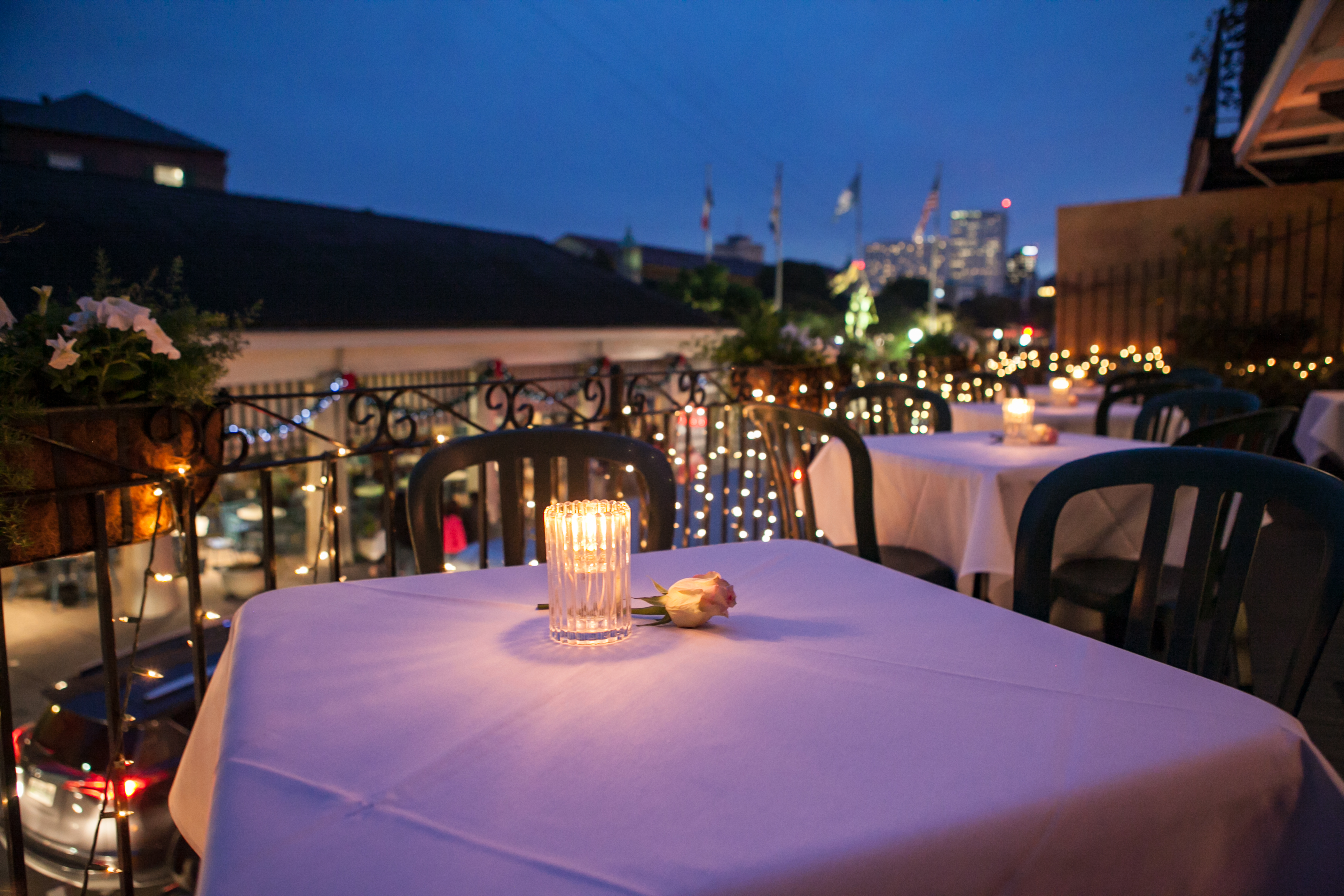 Evening on a terrace, lined up tables with table cloths, candle lights and a rose on each table