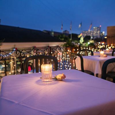 Evening on a terrace, lined up tables with table cloths, candle lights and a rose on each table