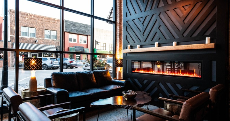 Interior with a fireplace, leather sofa, armchairs, and large window showing street view