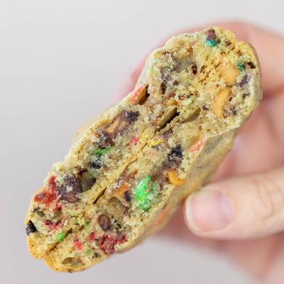 A hand holding a chocolate chip cookie with colorful bits.