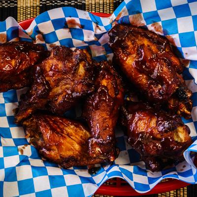 Barbecue chicken wings on blue and white checkered paper in a red basket.