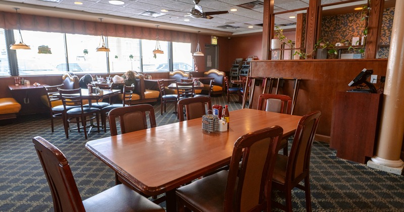 Interior of a warmly lit restaurant with wooden tables and booths by large windows