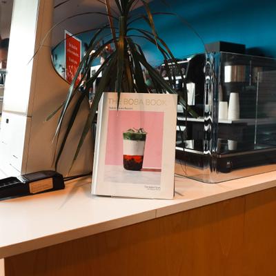 Counter display with a potted plant, espresso machine and a boba cookbook.