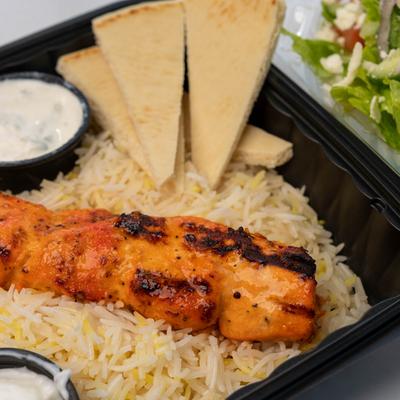 Chicken Kabob served over a bed of rice with sauce dips and pita