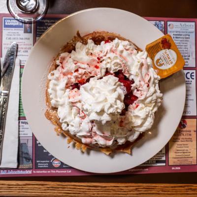 Waffle with whipped cream, strawberries and a small syrup container on the side.