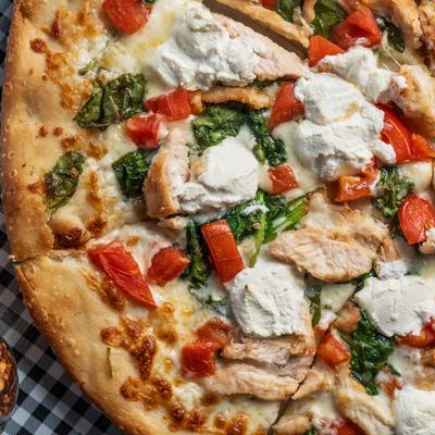 Close-up of a pizza topped with chicken, tomatoes, spinach, and dollops of ricotta.