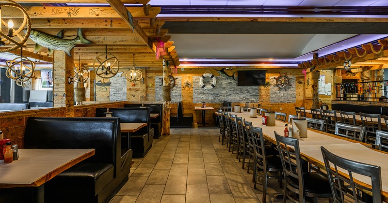 A rustic interior - wooden beams, black leather booths, a long wooden table, nautical decorations
