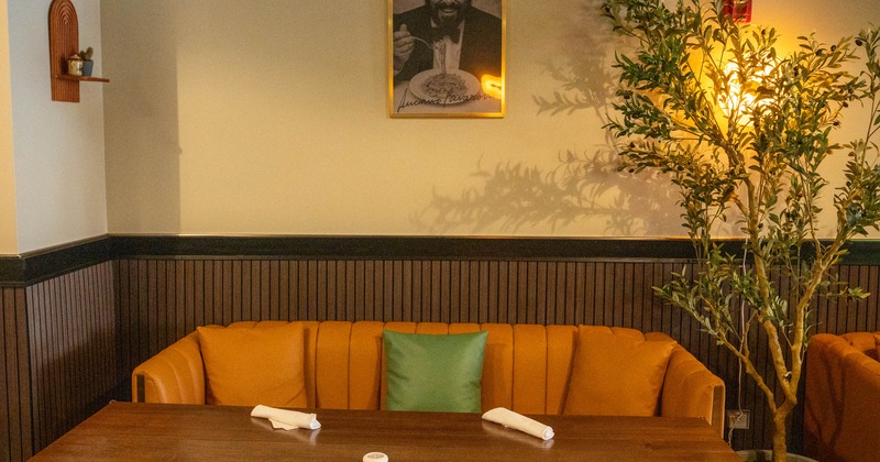 Dining area - a wooden table, orange seating, a framed photo on the wall and a potted plant
