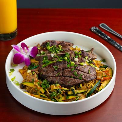 Veggie Bowl topped with sliced steak, garnished with fresh herbs and green onion.