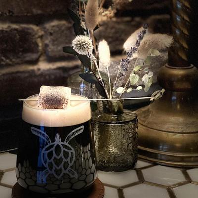 Stout beer served in a glass with turtle logo, garnished with burnt marshmallow