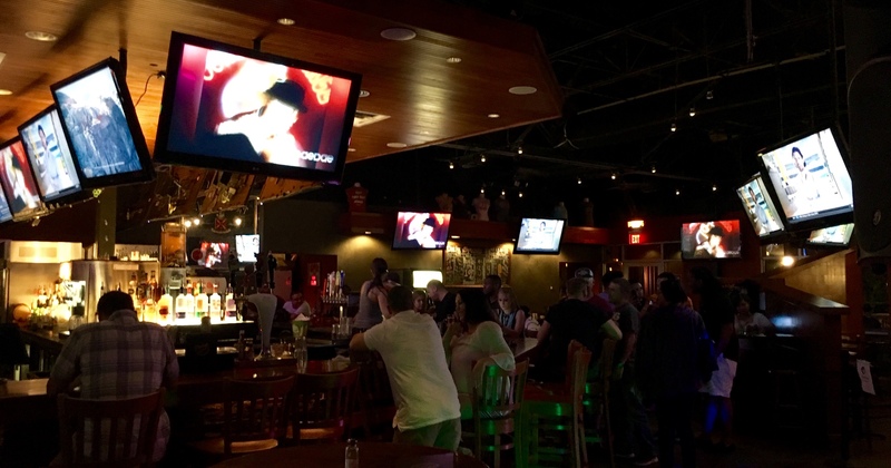 Interior, lots of guests sitting in the dim lighted bar area, large wall TV screens