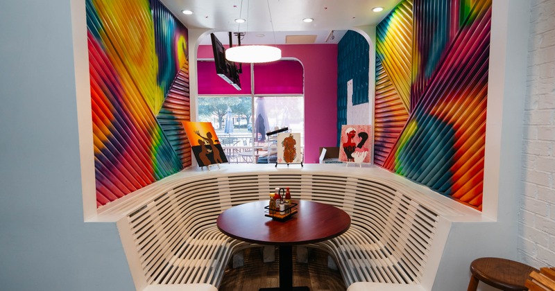 Interior, colorful corrugated walls, curved white bench, dark table and vibrant artwork