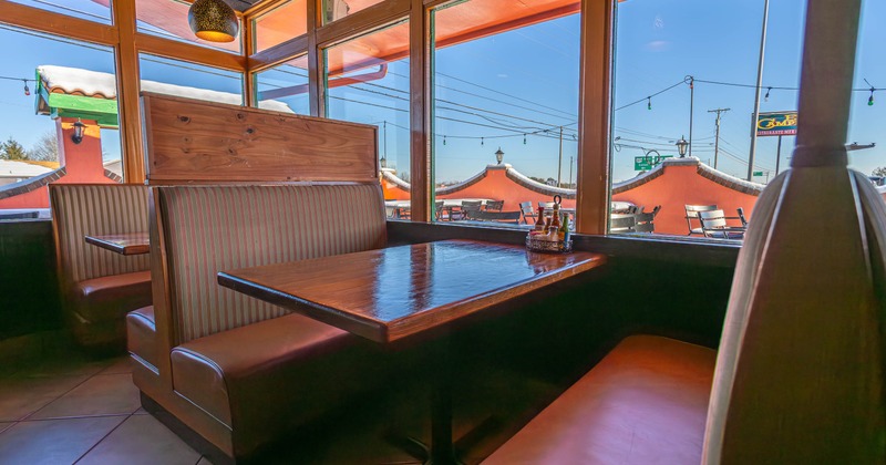 Interior of a restaurant booth with wooden tables and leather benches next to large windows