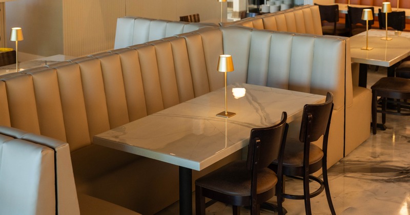 Modern dining area with beige booth seating, marble-like tables, and small gold lamps