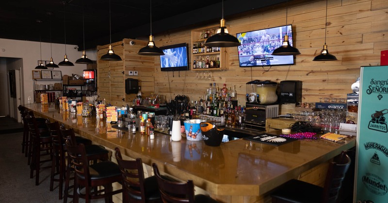 Interior, bar with a long wooden counter, pendant lights, and mounted TVs