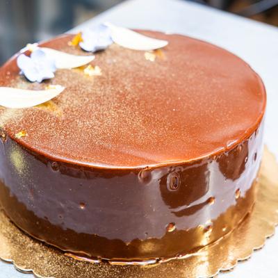 Chocolate cake covered in a glossy mirror glaze on a gold scalloped cake board.