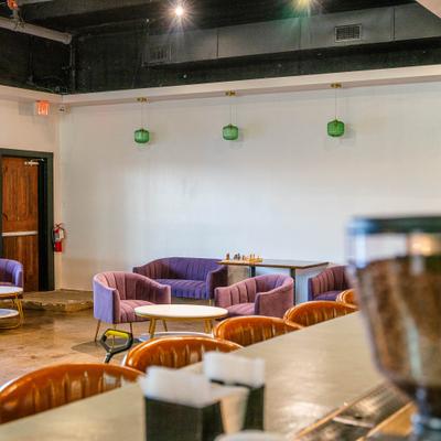 Interior featuring purple velvet armchairs, modern lighting and a bar counter with stools.