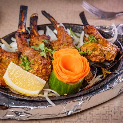 Lamb Chops Tandori served in a skillet with lemon wedge and sliced onions.