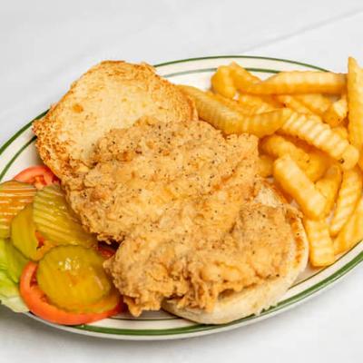 Fried chicken sandwich with crinkle-cut fries, pickles, lettuce, and tomato on the side.