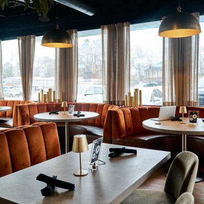 Restaurant interior with orange banquette seating, round tables, and large windows.