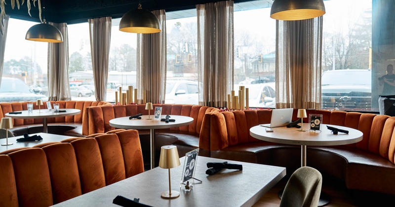 Restaurant interior with orange banquette seating, round tables, and large windows