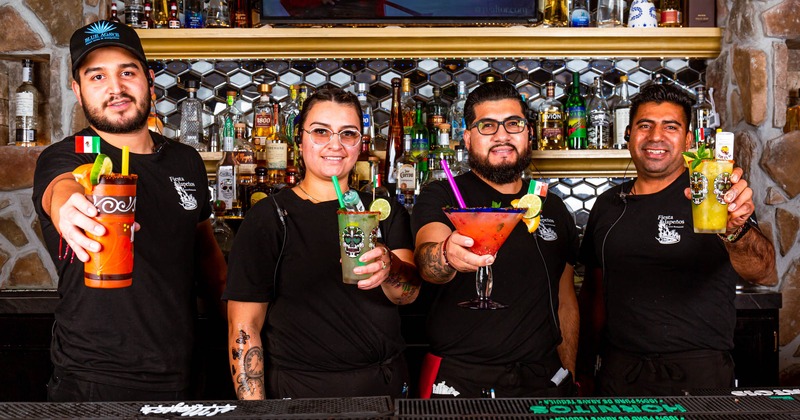 Interior, restaurant staff posing behind the counter, holding various drinks