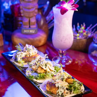 Street tacos  served on a black platter alongside a tropical cocktail.