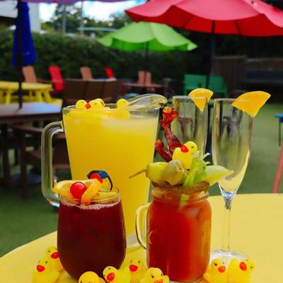 Colorful drinks with fruit garnishes and small rubber ducks on a yellow table.