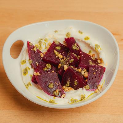 A white plate holds a salad of roasted beets with whipped ricotta, pesto, and nuts.