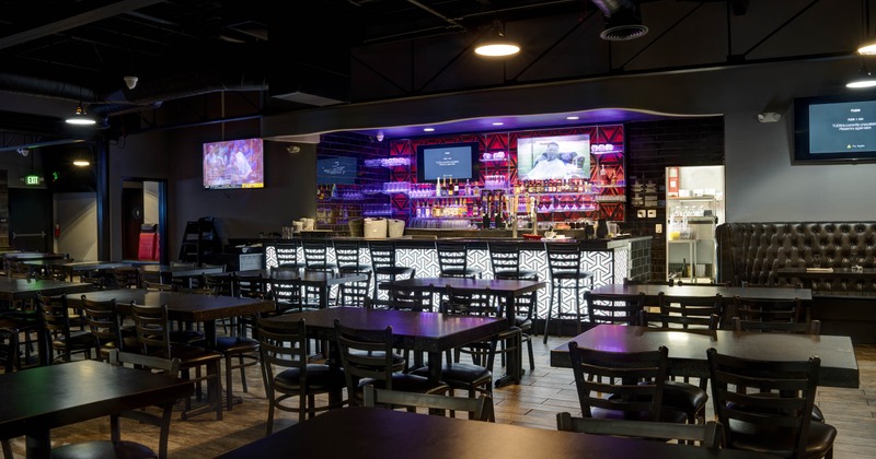Interior, tables and chairs in the foreground and an illuminated bar counter in the background