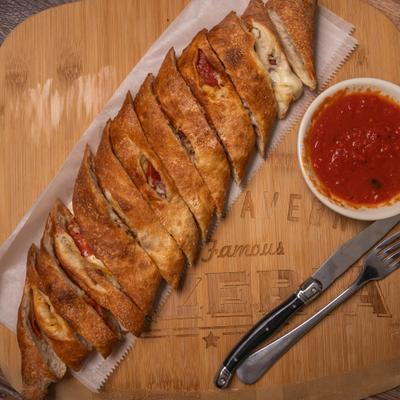 Sliced calzone with marinara sauce on a wooden serving board.
