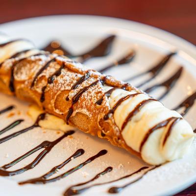 A single cannoli drizzled with chocolate, close up.