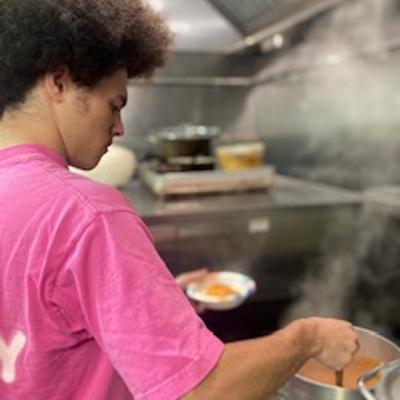 A person cooking in at a stove in the steaming restaurant's kitchen