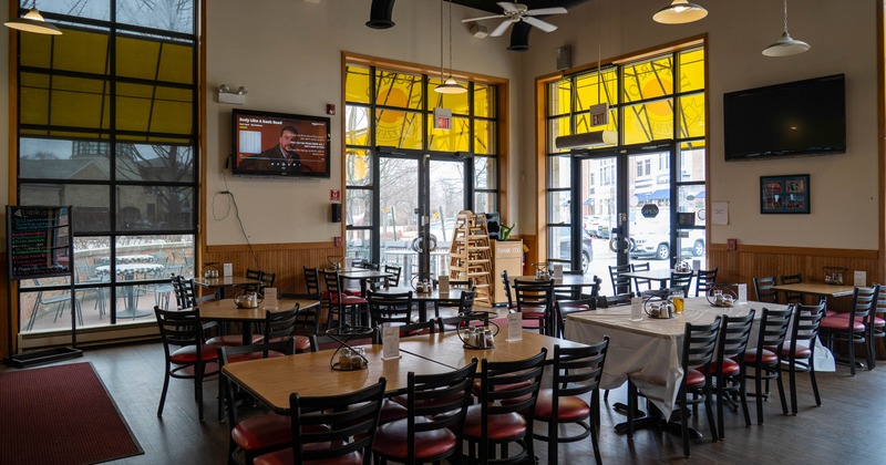 Interior with tables, chairs, large windows and TV screens.