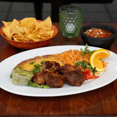 Steak bites, served with tomato, scallions, cilantro, guacamole, rice, and beans.