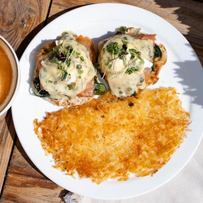 Lox Benedict with caper hollandaise sauce, microgreens, and crispy hash browns.