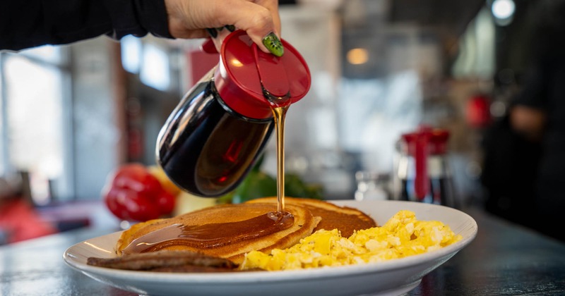 A hand pouring maple sauce on pancakes
