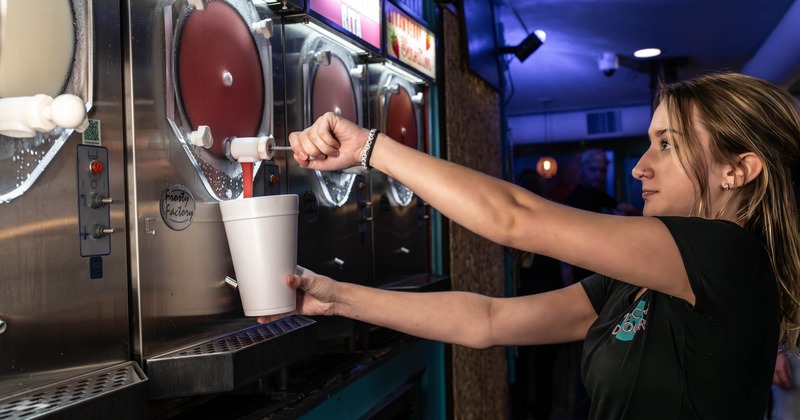 Bartender pours a glass of drink from a daiquiri dispenser