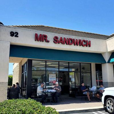 Outdoor view of Mr. Sandwich shop, people sitting at tables, a bright, sunny day.