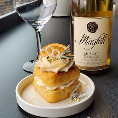 A dessert with cream frosting on a white plate, wine bottle, and an empty glass.
