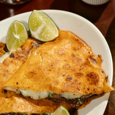 Jumbo quesabirria tacos served with lime wedges, close-up.