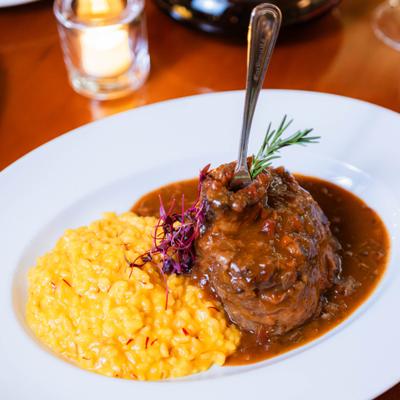 Braised beef with risotto, brown sauce, and rosemary garnish.
