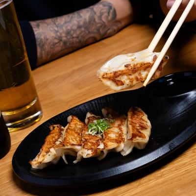 A person eating pan seared gyoza, accompanied with a beer.
