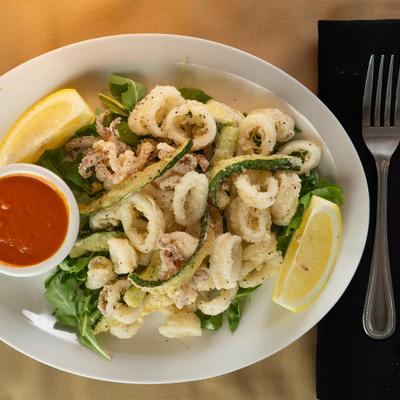 Calamari accompanied by fried zucchini, dipping sauce and lemon wedges.