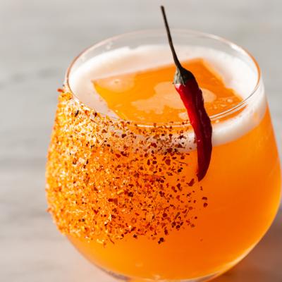 Orange cocktail drink with spicy rim and a red chili pepper garnish