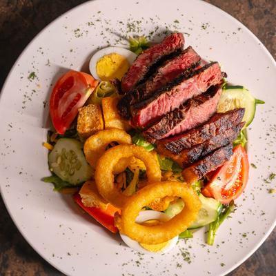 Steak salad, with mixed greens, cucumber, tomato, cheddar, egg, croutons, and onion rings.