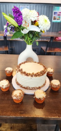 A decorated cake surrounded by cupcakes on a wooden table with flowers