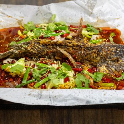 Whole spicy grilled fish topped with chilies, herbs, and vegetables.